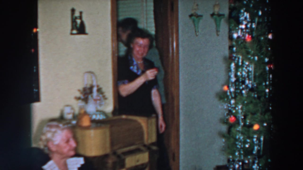 1957 Wheeling, Ohio home-movie frame with a woman in a doorway, an older seated woman, and a decorated Christmas tree in a private room.