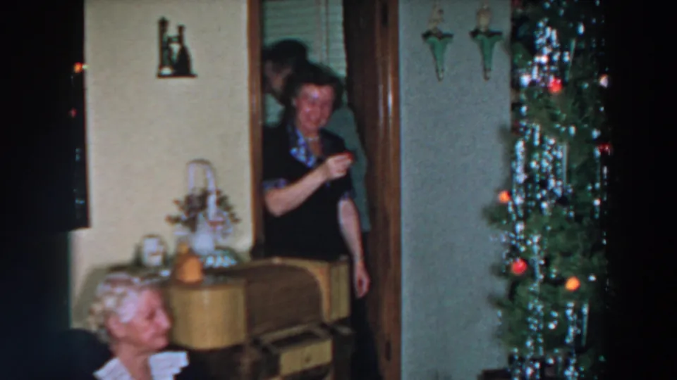 1957 Wheeling, Ohio home-movie frame with a woman in a doorway, an older seated woman, and a decorated Christmas tree in a private room.