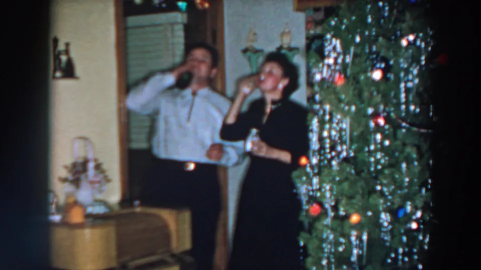 In this 1957 Wheeling, Ohio home-movie frame, the adults drink from glasses beside a tinsel-covered Christmas tree.