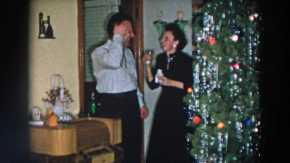 The man drinks from his glass while the woman holds hers beside the Christmas tree in the 1957 Wheeling, Ohio celebration.