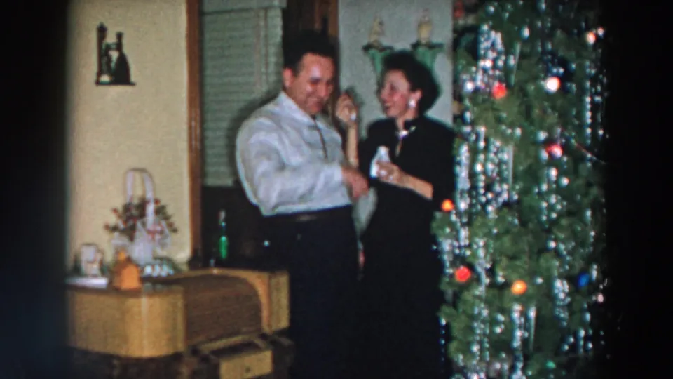 In 1957 Wheeling, Ohio home-movie footage, a man and woman stand near a tinsel-covered Christmas tree inside a private living room.