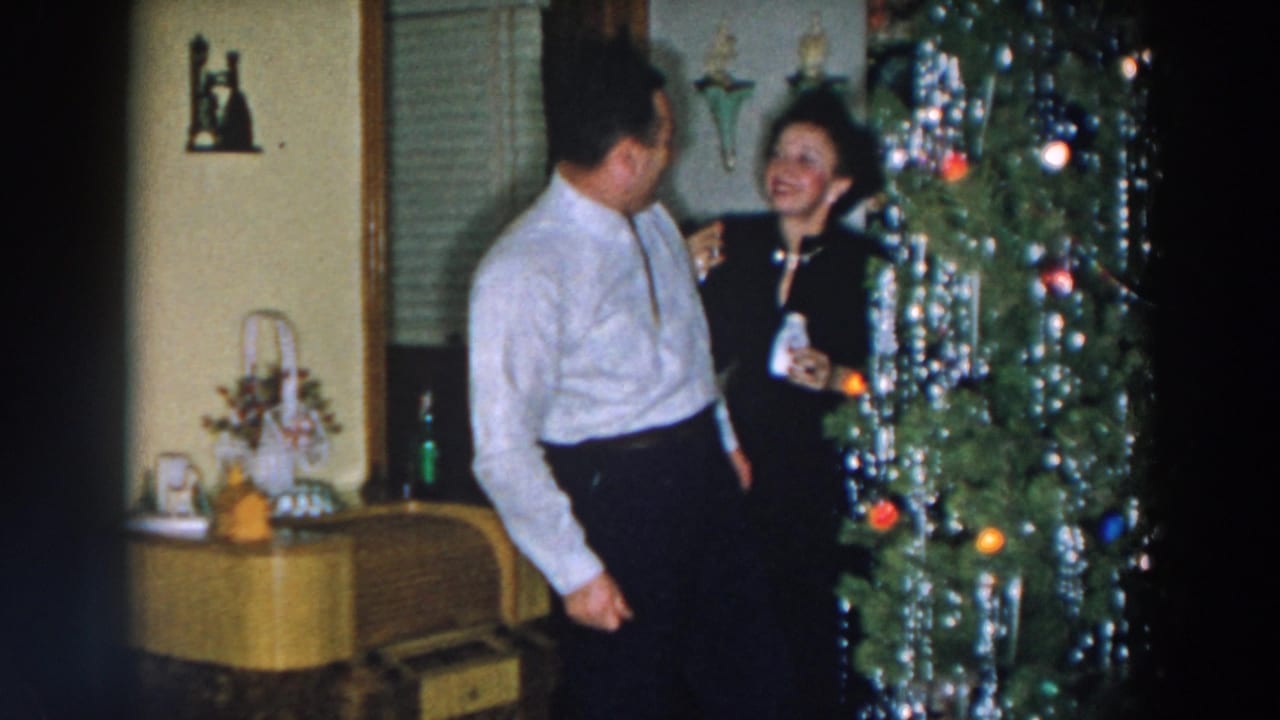 Couple smiling beside a decorated Christmas tree with a sideboard behind them.