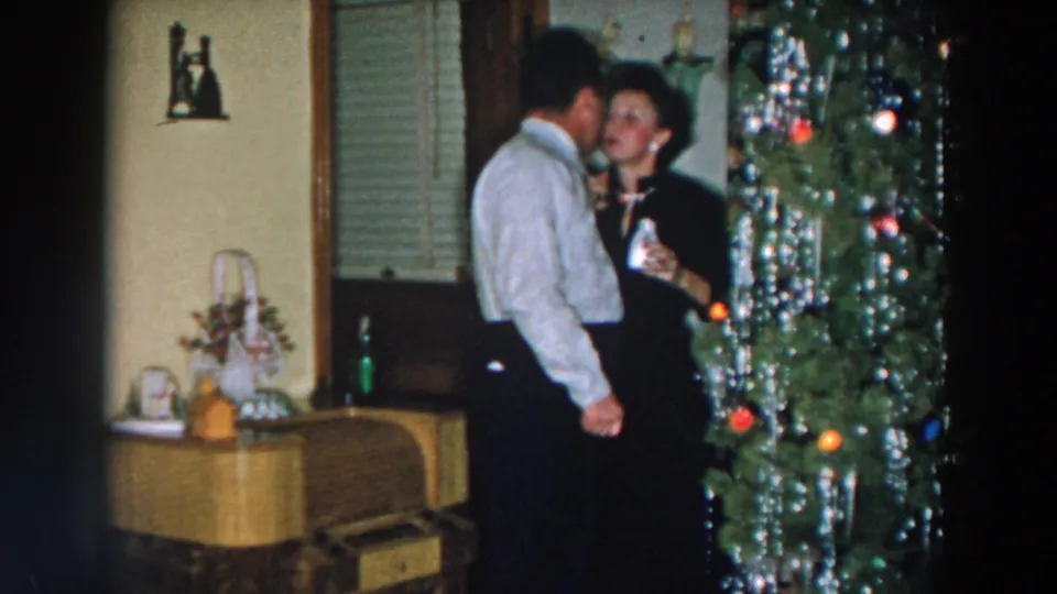A man leans close to a woman near a decorated Christmas tree during a 1957 home gathering in Wheeling, Ohio.
