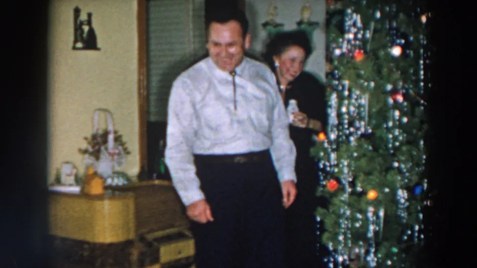 The man steps toward the camera while the woman smiles near the decorated tree in this Wheeling, Ohio Christmas home movie frame.