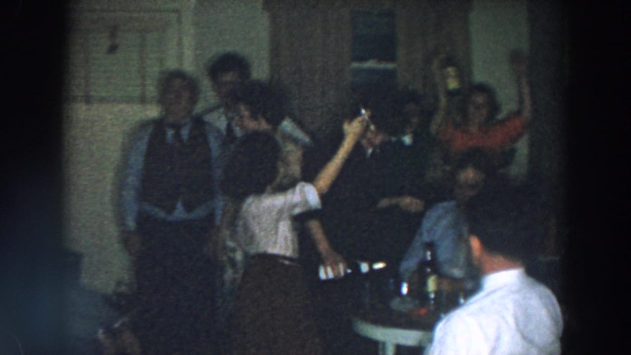 Adults stand and sit in a room as a woman raises a bottle above shoulder height.