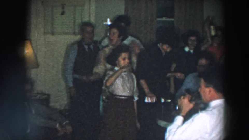 Home-movie view of a dim 1957 Wheeling, Ohio party, with adults gathered around tables and drinks in a private interior.