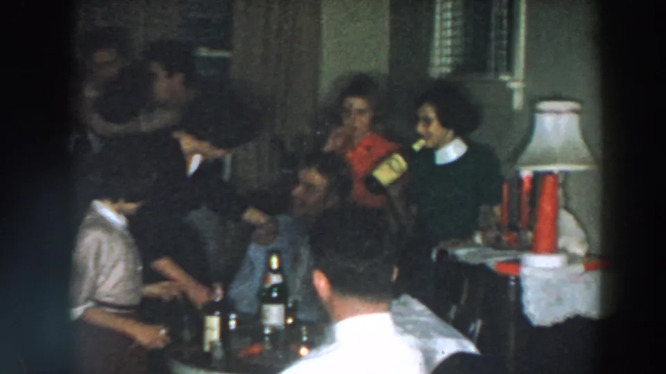 Adults socialize around a table with bottles during a 1957 Wheeling, Ohio home party, with a lamp and doorway visible.