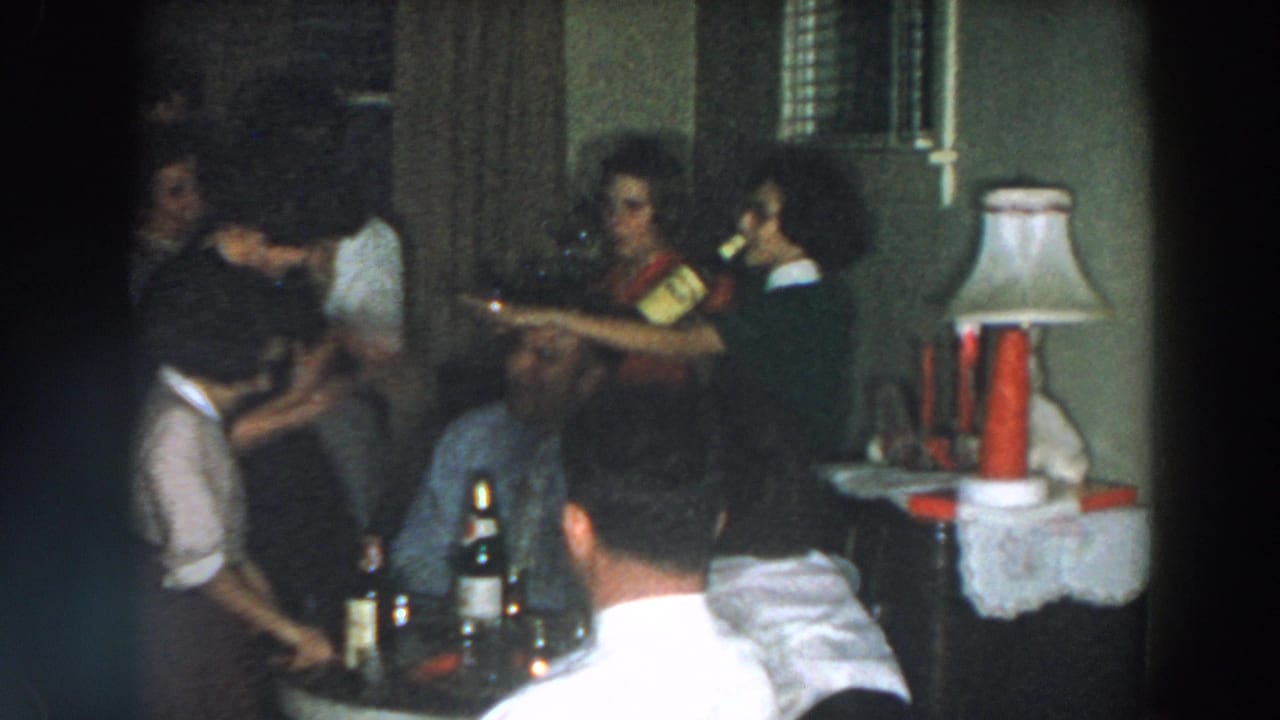 Party guests stand near a table while a woman holds a bottle.