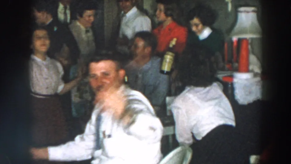 A crowded 1957 home party scene shows adults near a table, a woman in red, and a seated man gesturing toward the camera.