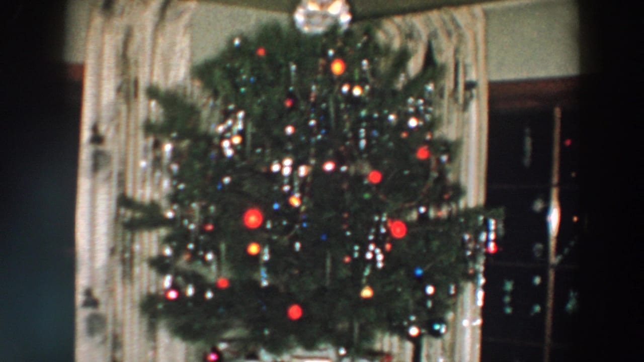 Decorated Christmas tree with tinsel, colored ornaments, and curtains behind it.