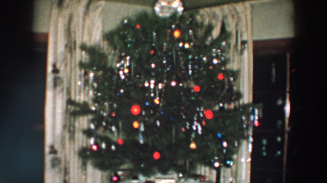 1957 Wheeling, Ohio frame of a lit Christmas tree with reflective tinsel, red ornaments, and a visible tree topper inside a private home.