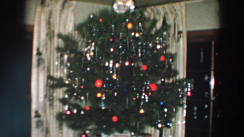 1957 Wheeling, Ohio 8mm frame showing a softly focused Christmas tree with red ornaments, tinsel, lights, and curtains behind it.