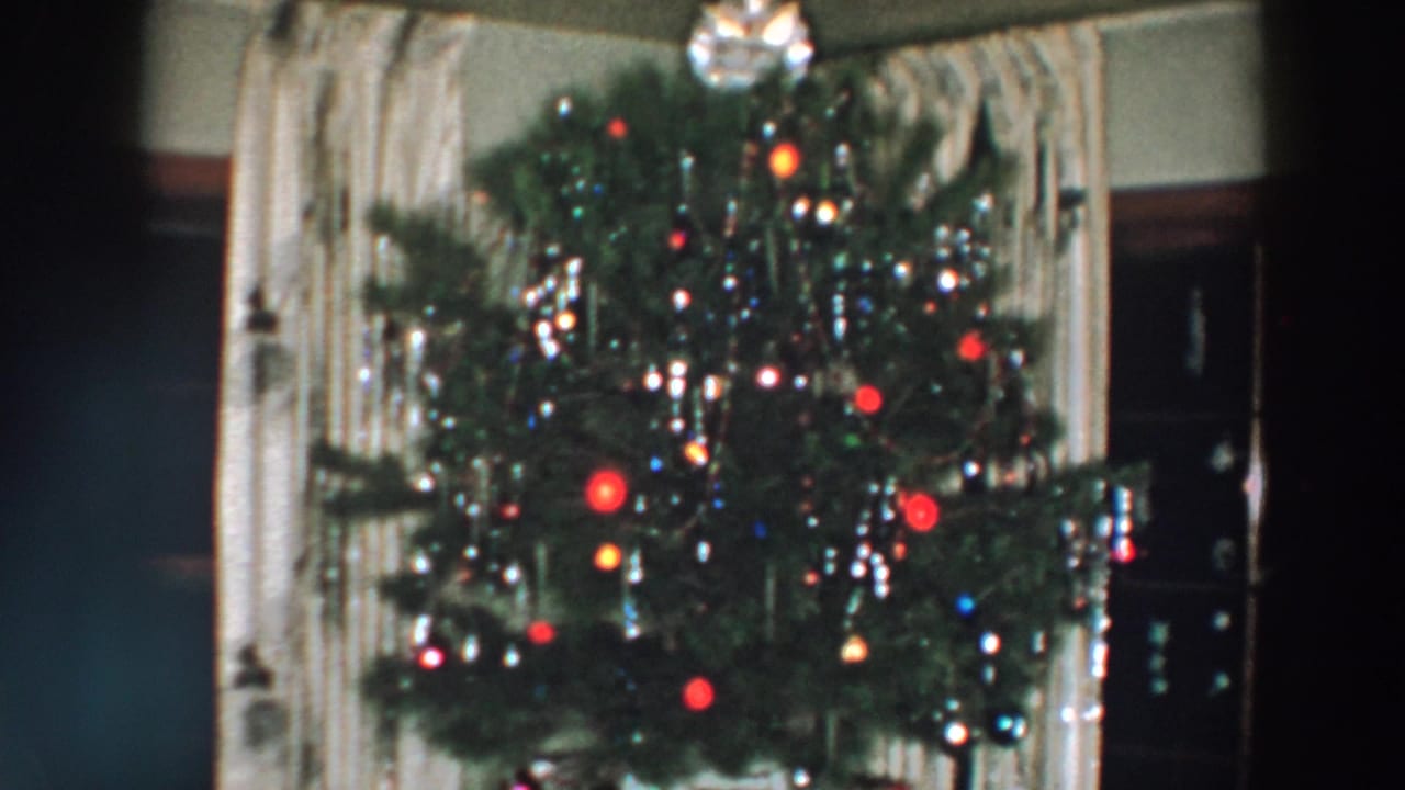 Christmas tree with colored lights, tinsel, ornaments, curtains, and dark furniture.