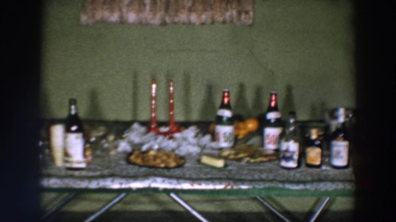 1957 Wheeling, Ohio home-movie frame of a holiday spread with red candles, alcohol bottles, food, oranges, and punch.