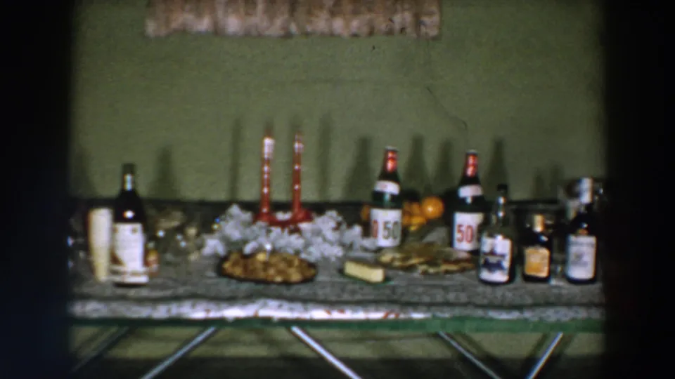 1957 Wheeling, Ohio home-movie frame showing a closer view of the holiday table with bottles, candles, food, and fruit.