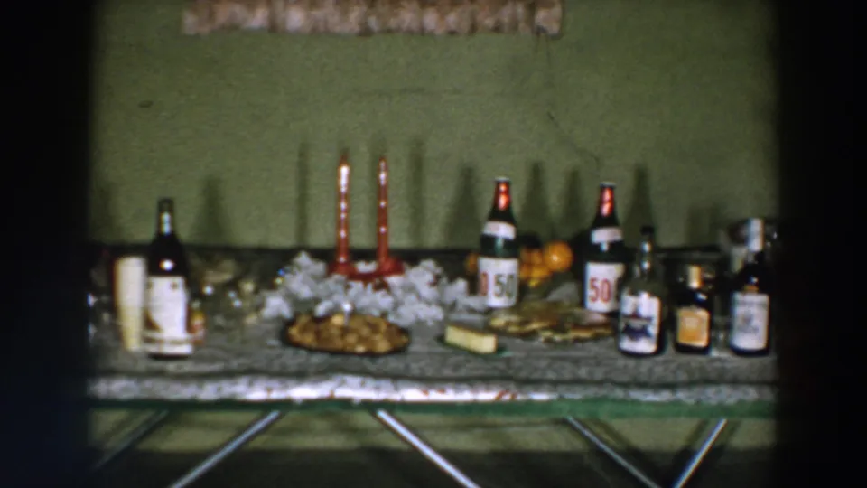 1957 Wheeling, Ohio home-movie frame of a decorated holiday table with alcohol bottles, candles, food, and fruit.