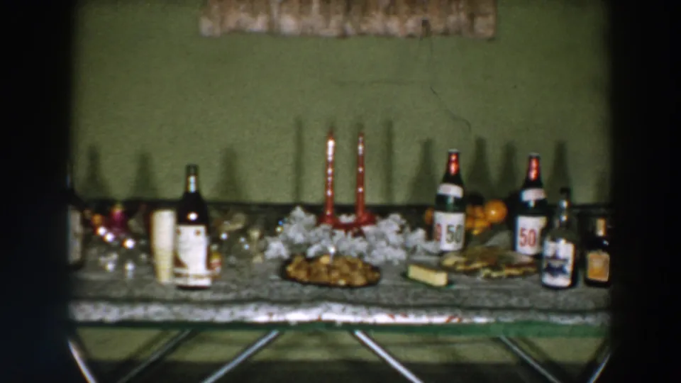 1957 Wheeling, Ohio home-movie frame showing a decorated serving table with beverage bottles, cups, candles, garland, and food.
