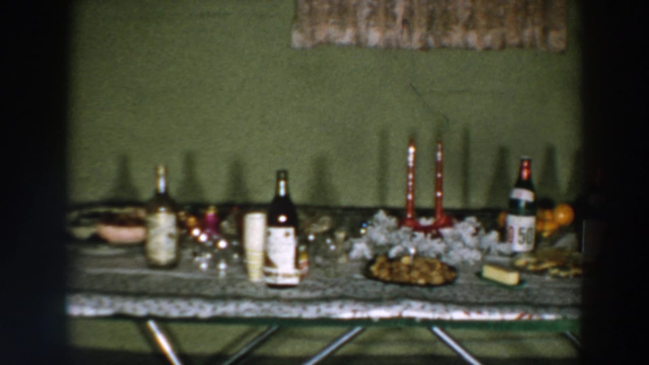 1957 Wheeling, Ohio frame of a party serving table with labeled bottles, red candles, white decorations, fruit, and food.