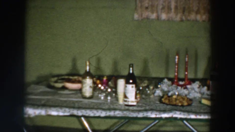 1957 Wheeling, Ohio home-movie still showing a decorated food-and-drink table with bottles, cups, candles, garland, and serving dishes.