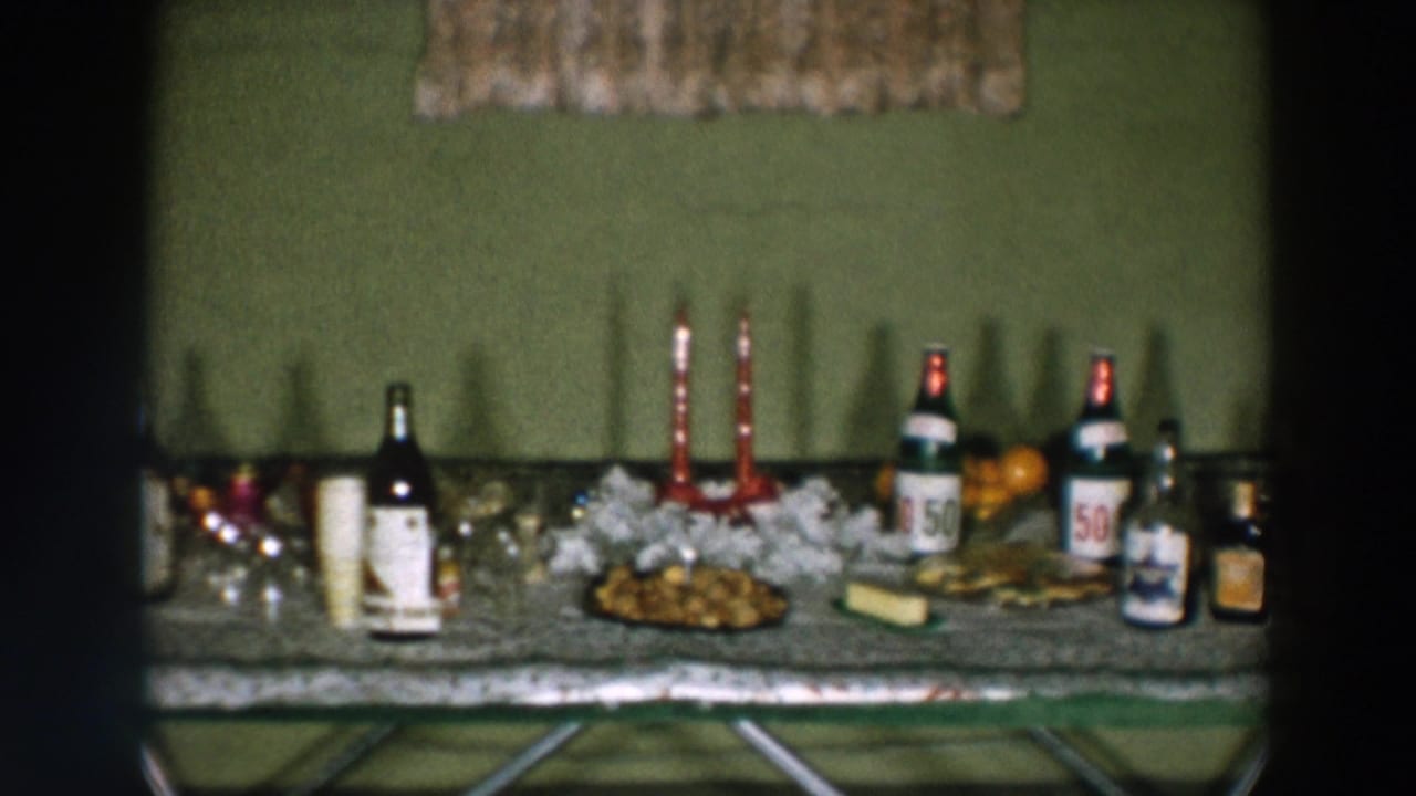 Party table with red candles, bottles, cups, oranges, snacks, and glassware against a green wall.