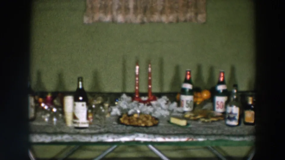 1957 Wheeling, Ohio home-movie frame with a holiday table set with bottles, red candles, cups, oranges, snacks, and glassware.