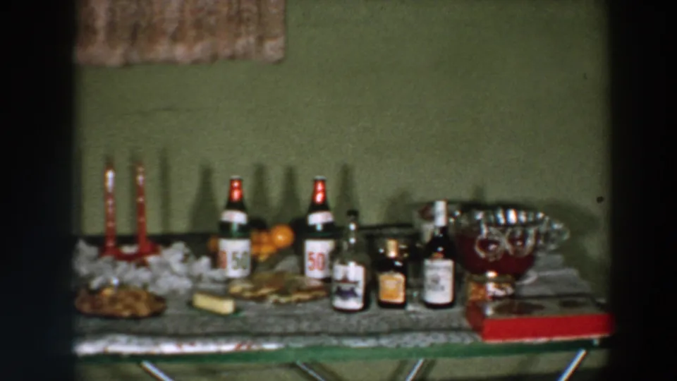 1957 Wheeling, Ohio home-movie frame showing a holiday table with red candles, bottles, snacks, oranges, and a large glass punch bowl.