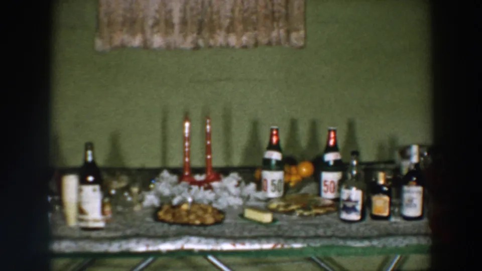 1957 Wheeling, Ohio frame of a decorated party table with visible bottle labels, candles, food, and fruit.
