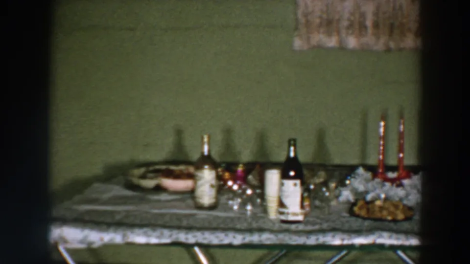 1957 Wheeling, Ohio frame showing the left portion of a home celebration table with drinks, glassware, candles, and food.