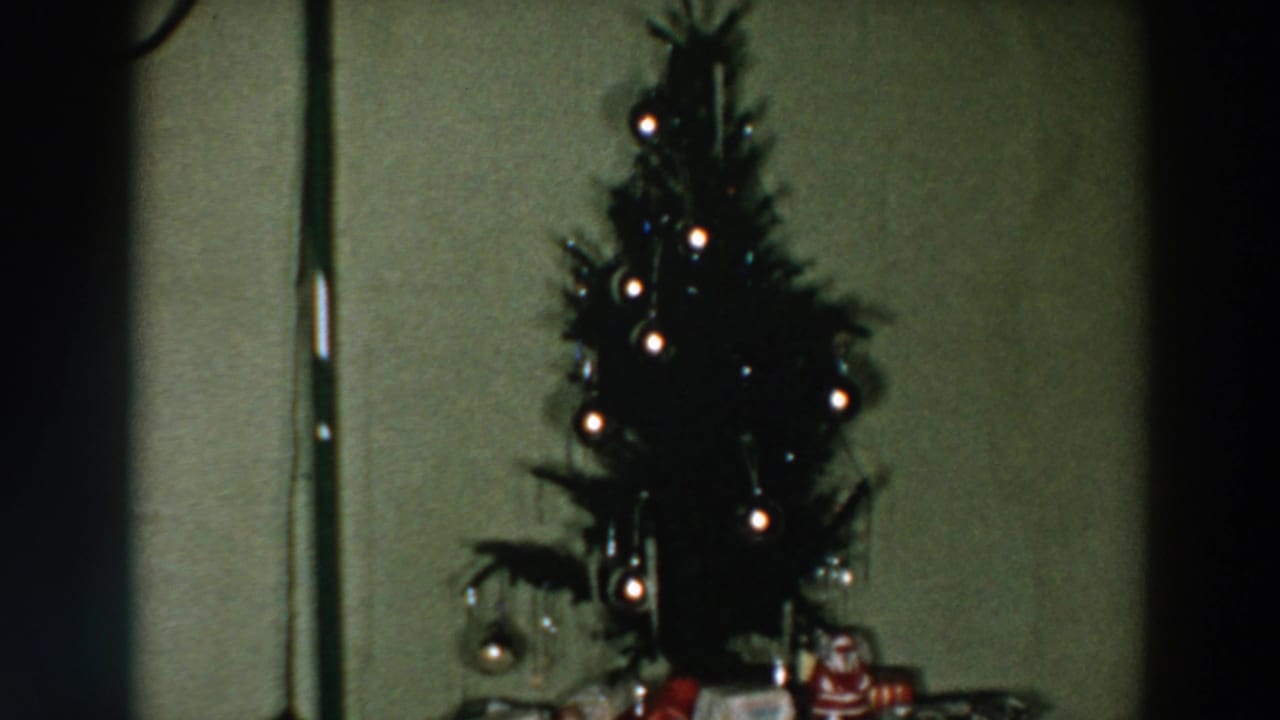Small lit Christmas tree on a table with wrapped gifts against a green wall.