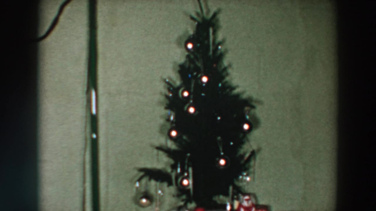 Lit tabletop Christmas tree with round ornaments and wrapped gifts in a 1957 Wheeling, Ohio home interior.