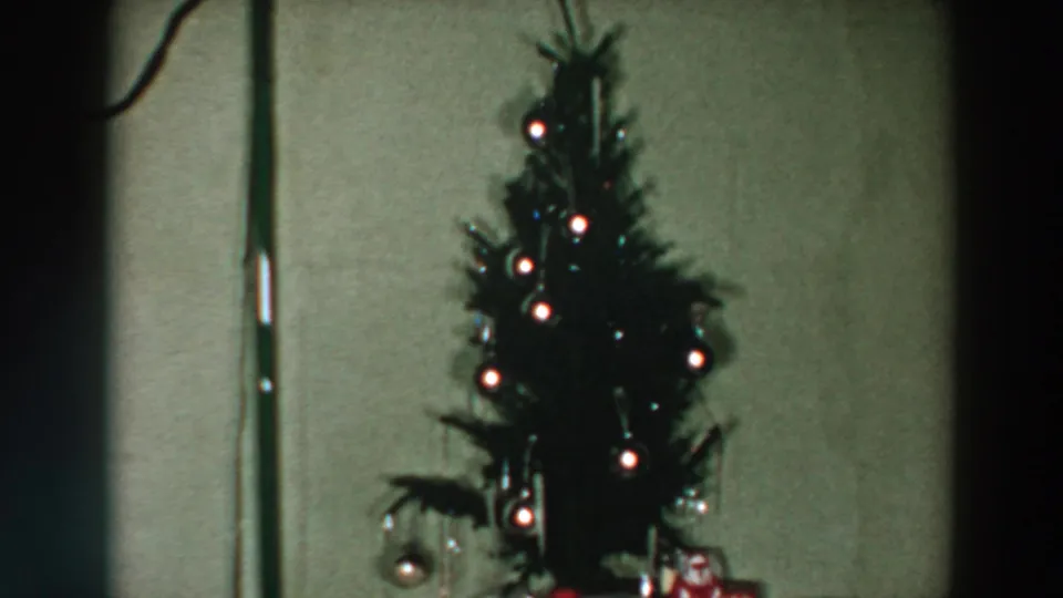 Lit tabletop Christmas tree with round ornaments and wrapped gifts in a 1957 Wheeling, Ohio home interior.