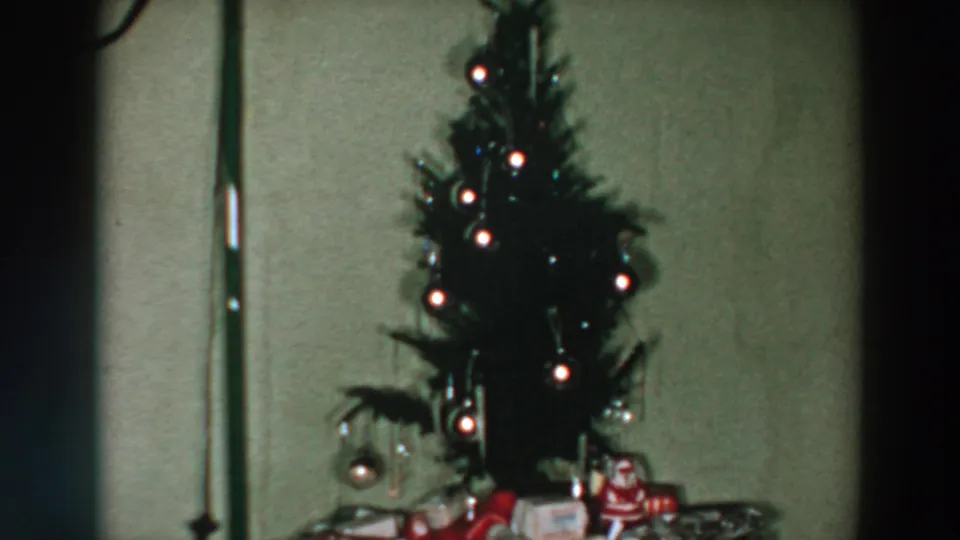 Soft-focus 8mm view of a small lit Christmas tree and wrapped gifts in a private Wheeling, Ohio home, 1957.