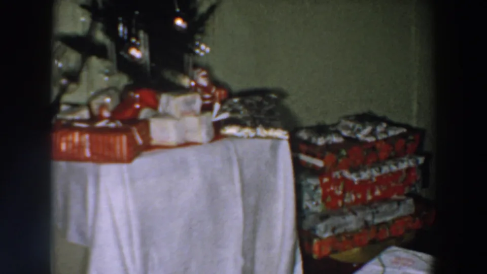 Close 1957 Wheeling, Ohio home-movie view of Christmas packages, a Santa figure, candles, and stacked patterned gift boxes.