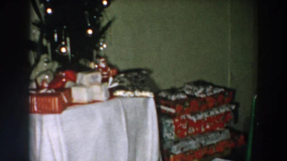 1957 Wheeling, Ohio 8mm frame showing stacked holiday presents, a white table covering, and part of a decorated tree.