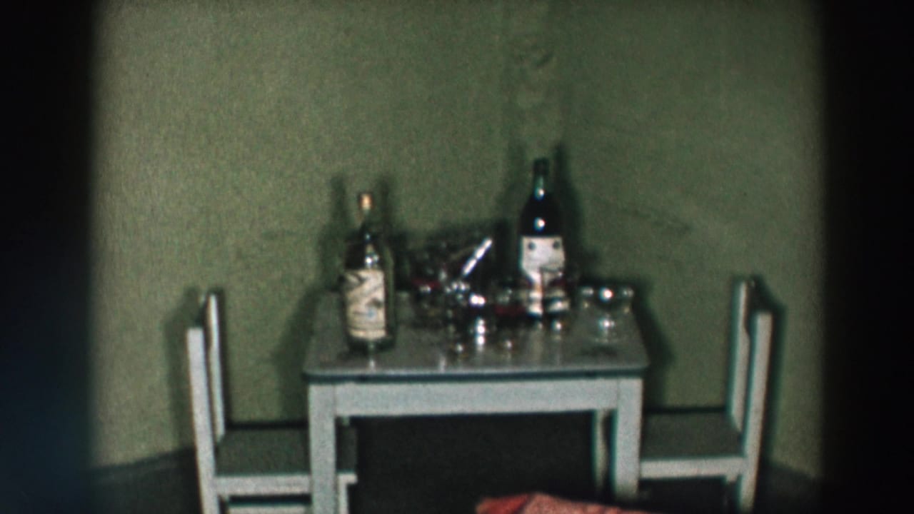 Small table with liquor bottles, glasses, shaker, and two chairs in a domestic interior.