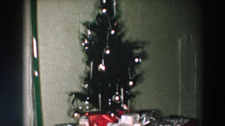 1957 Wheeling, Ohio home-movie frame showing a decorated Christmas tree with lights, ornaments, and wrapped presents beneath it.