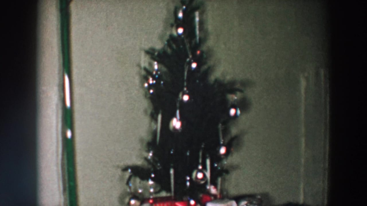 Small decorated Christmas tree beside wrapped presents in a dim private interior.