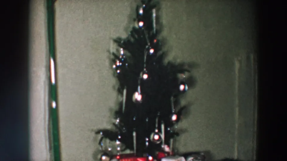 Small decorated Christmas tree with ornaments and wrapped presents in a 1957 Wheeling, Ohio home-movie interior.