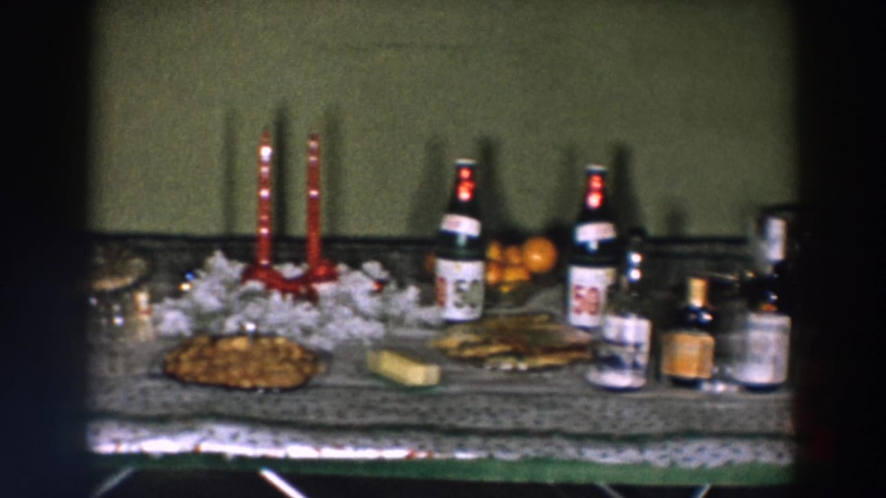 Table with red candles, bottled drinks, snacks, oranges, and small jars against a green wall.