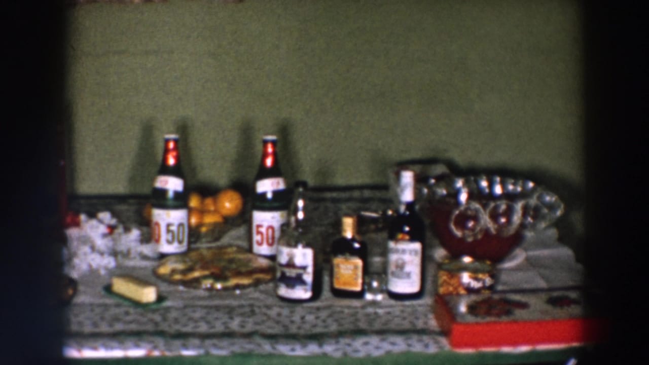 1957 Wheeling home-movie frame with labeled bottles, a snack platter, oranges, jars, and a glass punch bowl on a decorated table.