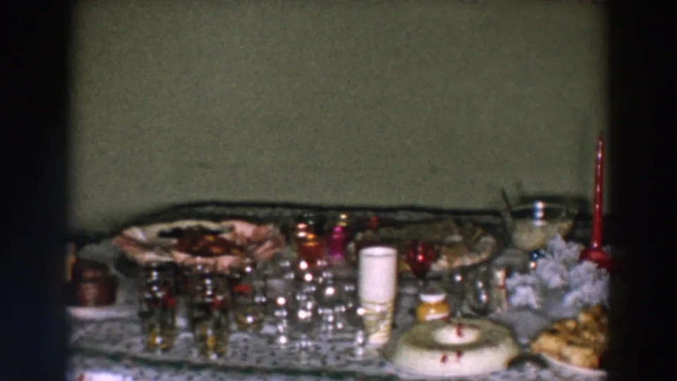 1957 Wheeling home-movie frame showing glassware, serving dishes, red candles, snacks, and a small decorated centerpiece on a party table.