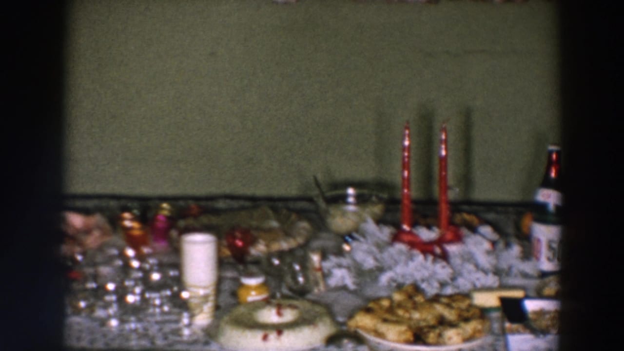 1957 Wheeling, Ohio home-movie frame showing a festive table with food, glassware, red candles, bottles, and a white wreath-like centerpiece.