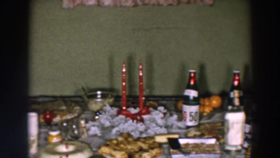 1957 home-movie frame from Wheeling, Ohio showing a full table with red candles, plated food, bottles, oranges, and a white centerpiece.