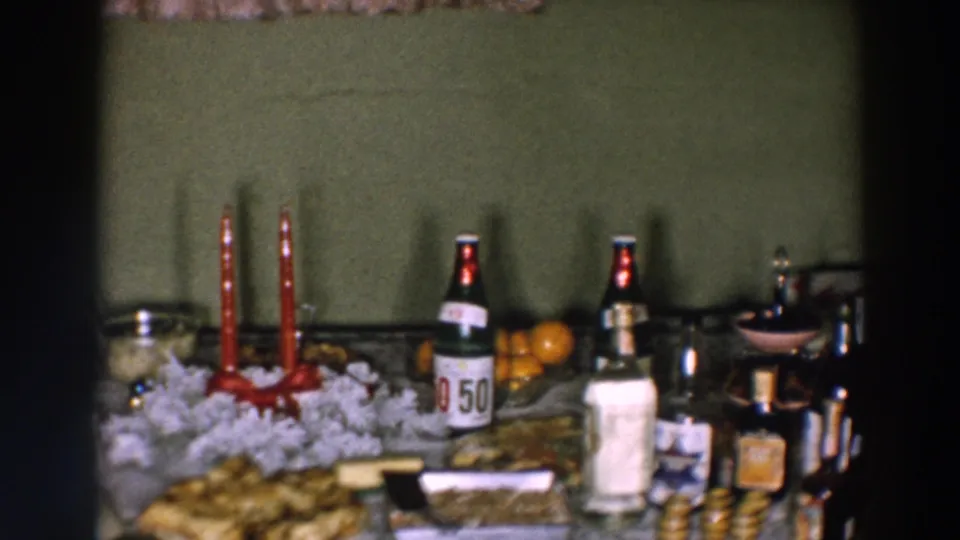 Wheeling, Ohio 1957 home-movie frame showing the right side of a festive table with candles, bottles, oranges, glassware, and serving dishes.