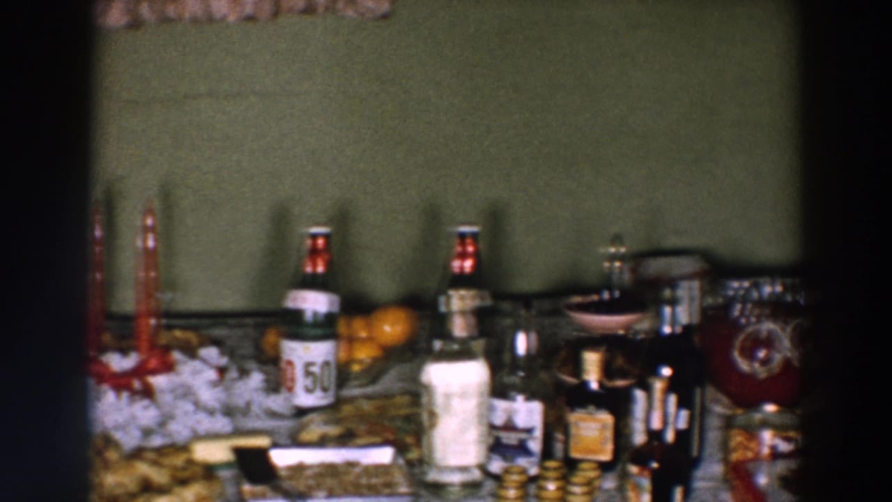1957 Wheeling, Ohio home-movie frame showing a prepared party table with red candles, desserts, bottles, oranges, and glassware.