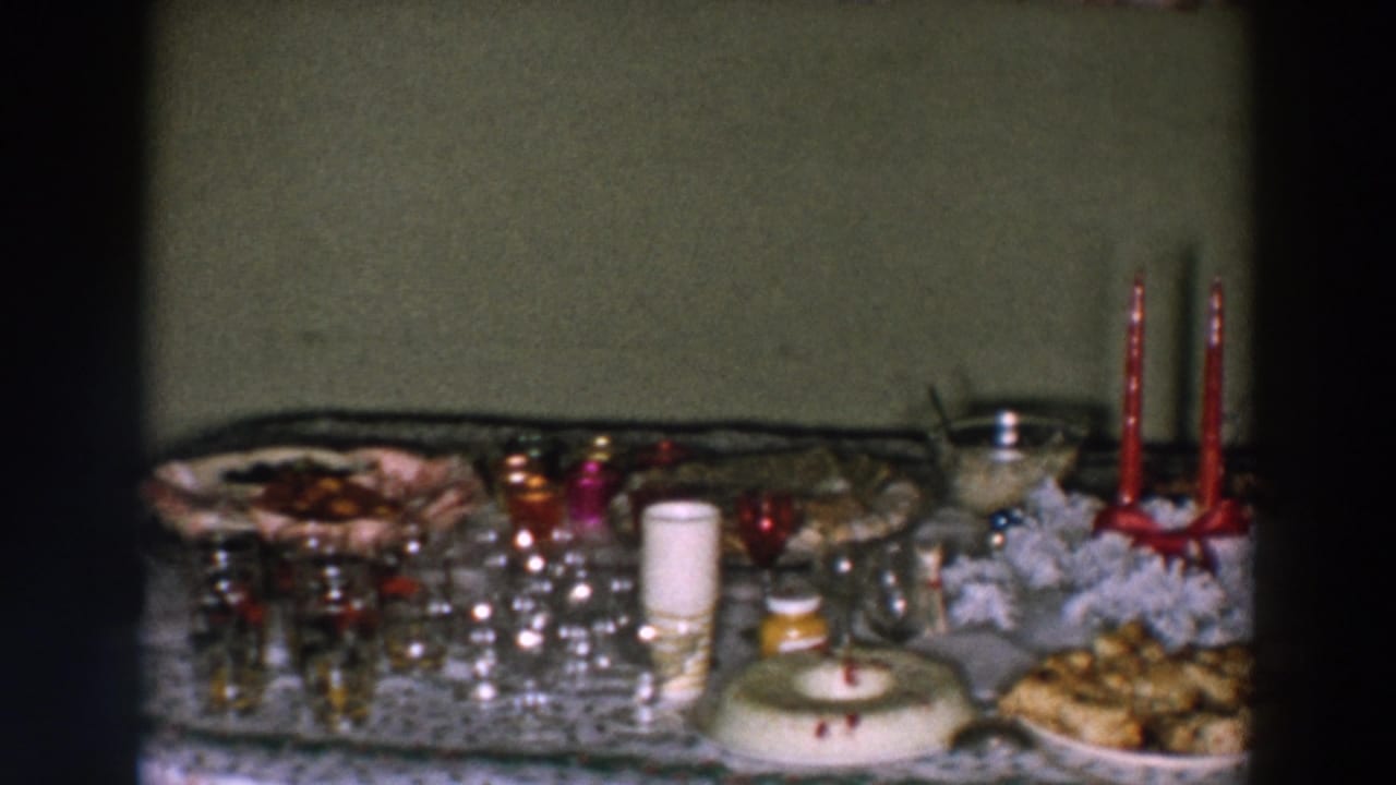 Lace-covered holiday table with glassware, food platters, red candles, and small decorations.