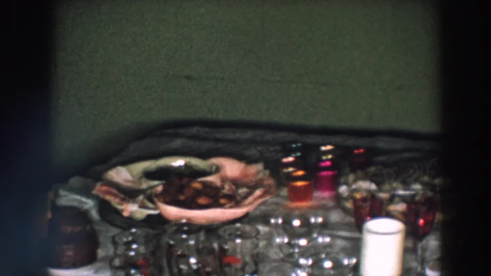 Final 1957 Wheeling, Ohio home-movie frame showing a close view of the festive table with food, glassware, decorations, and a white candle.
