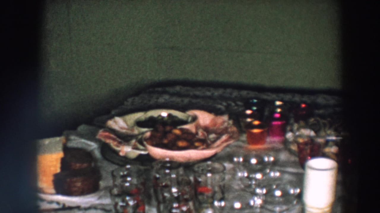 1957 Wheeling, Ohio home-movie frame showing a holiday dinner table with glassware, serving bowls, desserts, and red candles in soft 8mm focus.