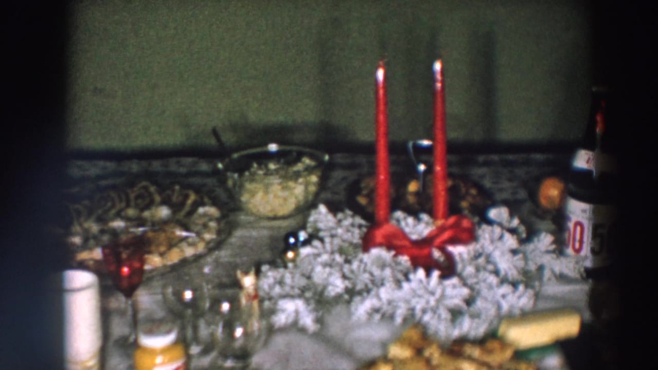 Holiday table detail from 1957 Wheeling, Ohio footage, centered on red candles, a frosted wreath, glassware, a serving bowl, and a partly visible bottle.
