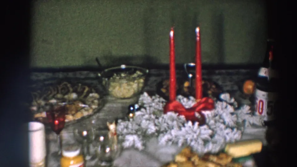 Holiday table detail from 1957 Wheeling, Ohio footage, centered on red candles, a frosted wreath, glassware, a serving bowl, and a partly visible bottle.